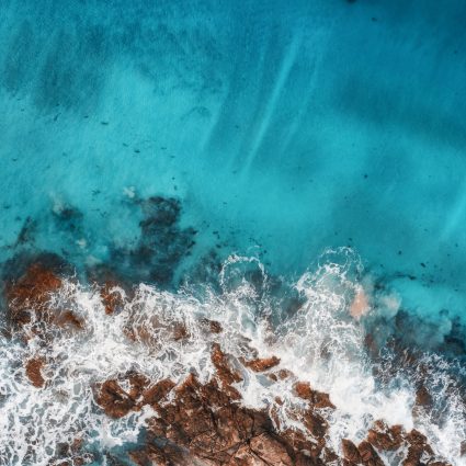 Aerial view of waves, rocks and transparent sea. Summer seascape with ocean, sandy beach, beautiful waves, cliffs, blue water at sunset. Top view from drone. Rocky coastline. Travel. Maldives. Concept