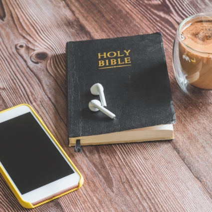The Holy Bible with headphones, a phone and a hot cup of coffee. Reading the bible. Concept for faith, spirituality and religion.