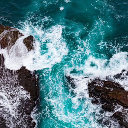 Aerial view seascape of big dynamic surf waves crashing turbulent onto rocky shore nature abstract background pattern