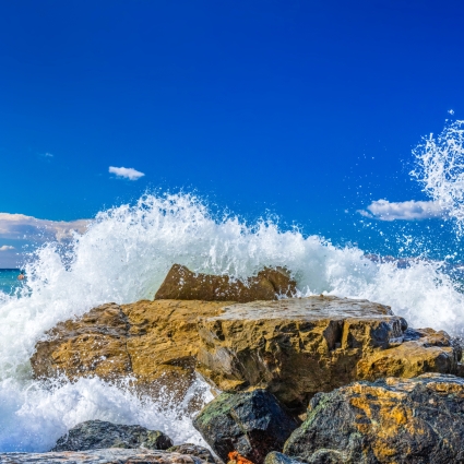 Waves crash and splash on rocks on sunny blue sky